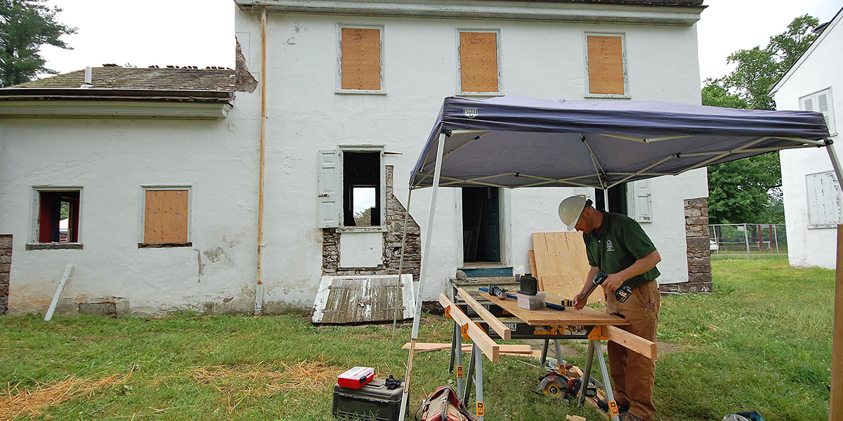 A man works in front of a historic building, which has boarded-up windows while undergoing maintenance.